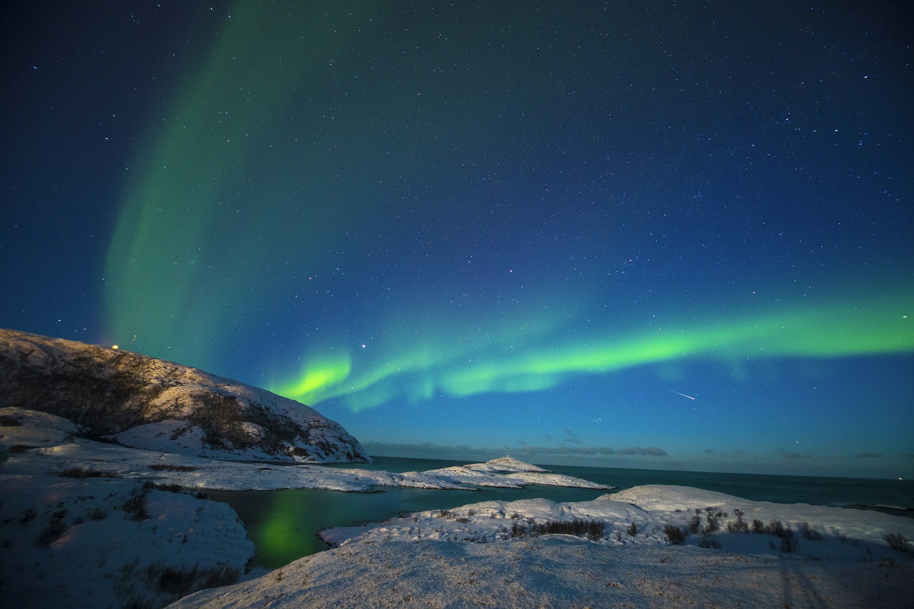Grünes Nordlicht über Wasser und Bergen bei Tromsø